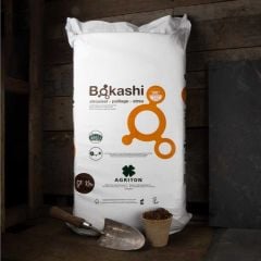 white bag filled with bokashi bran stood upright in a shed with a potting trowel and seedling pot in front 